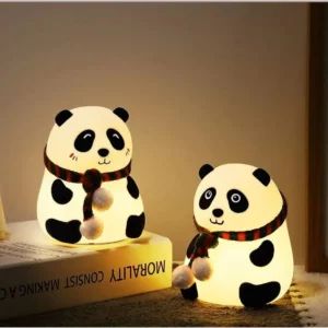 Veilleuse panda en silicone souple avec foulard festif sur une table de chevet, allumée avec une lumière chaude